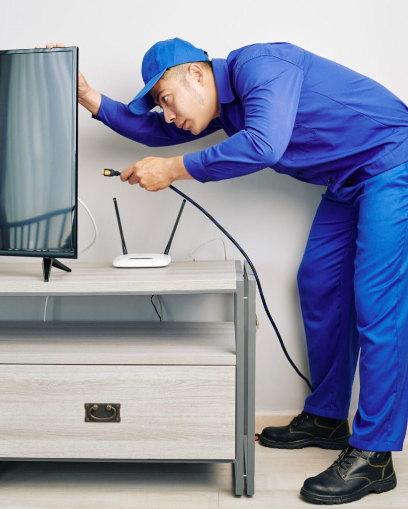 Serious young Vietnamese repairman installing tv set in apartment of customer