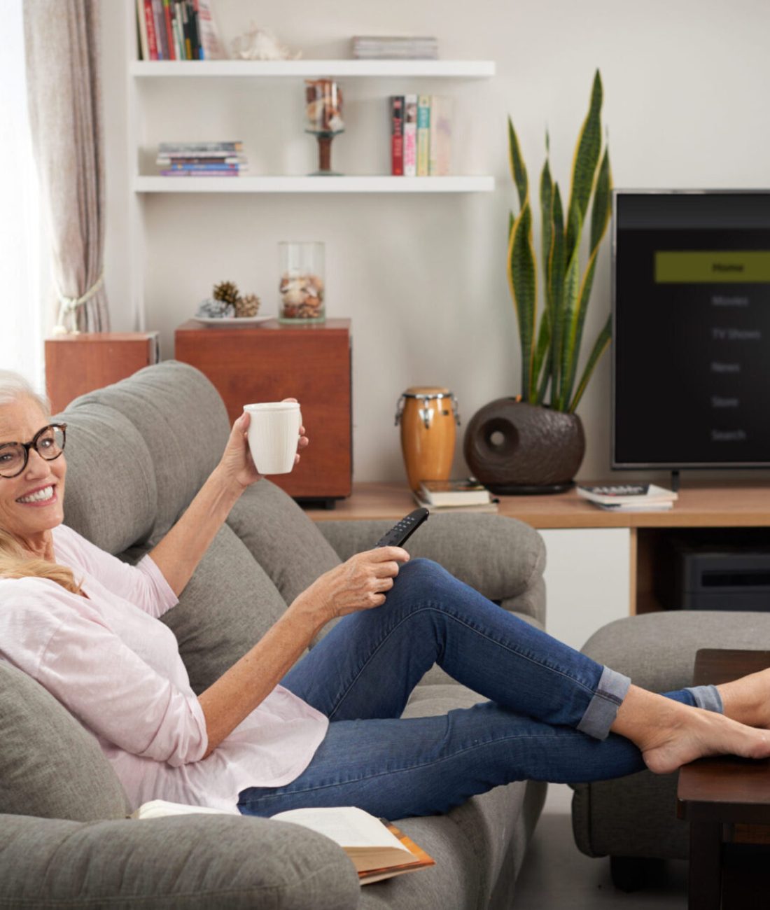 Happy senior woman drinking tea and watching tv at home